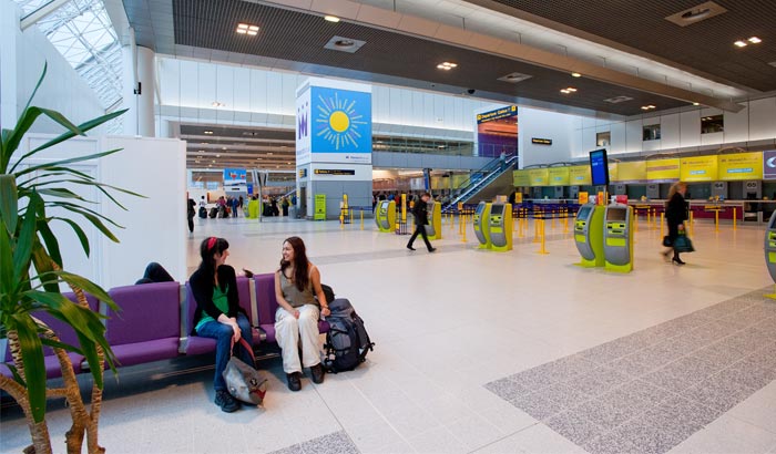 Two women converse in the Manchester Airport Terminal 2 under LED ceiling lighting