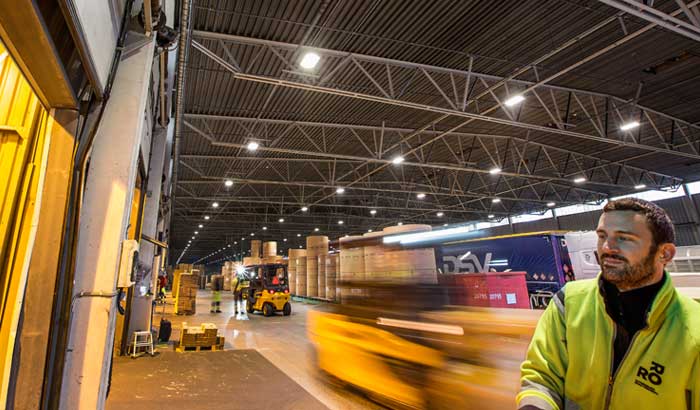 Warehouse worker with moving forklift and truck in background